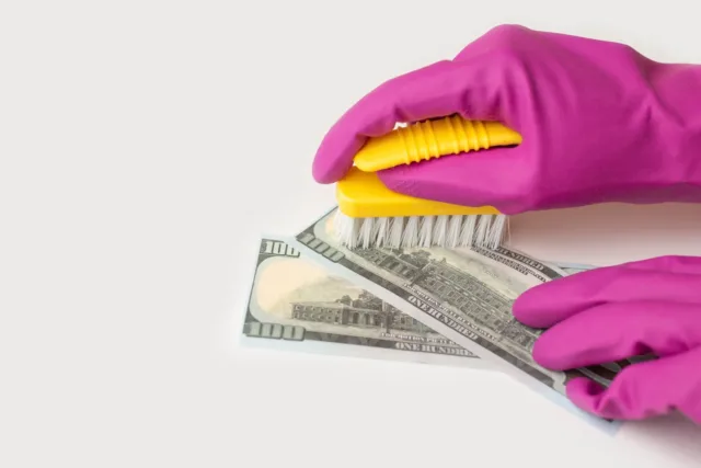 Dłonie w różowych rękawiczkach przy pomocy szczotki, czyszczą banknoty.